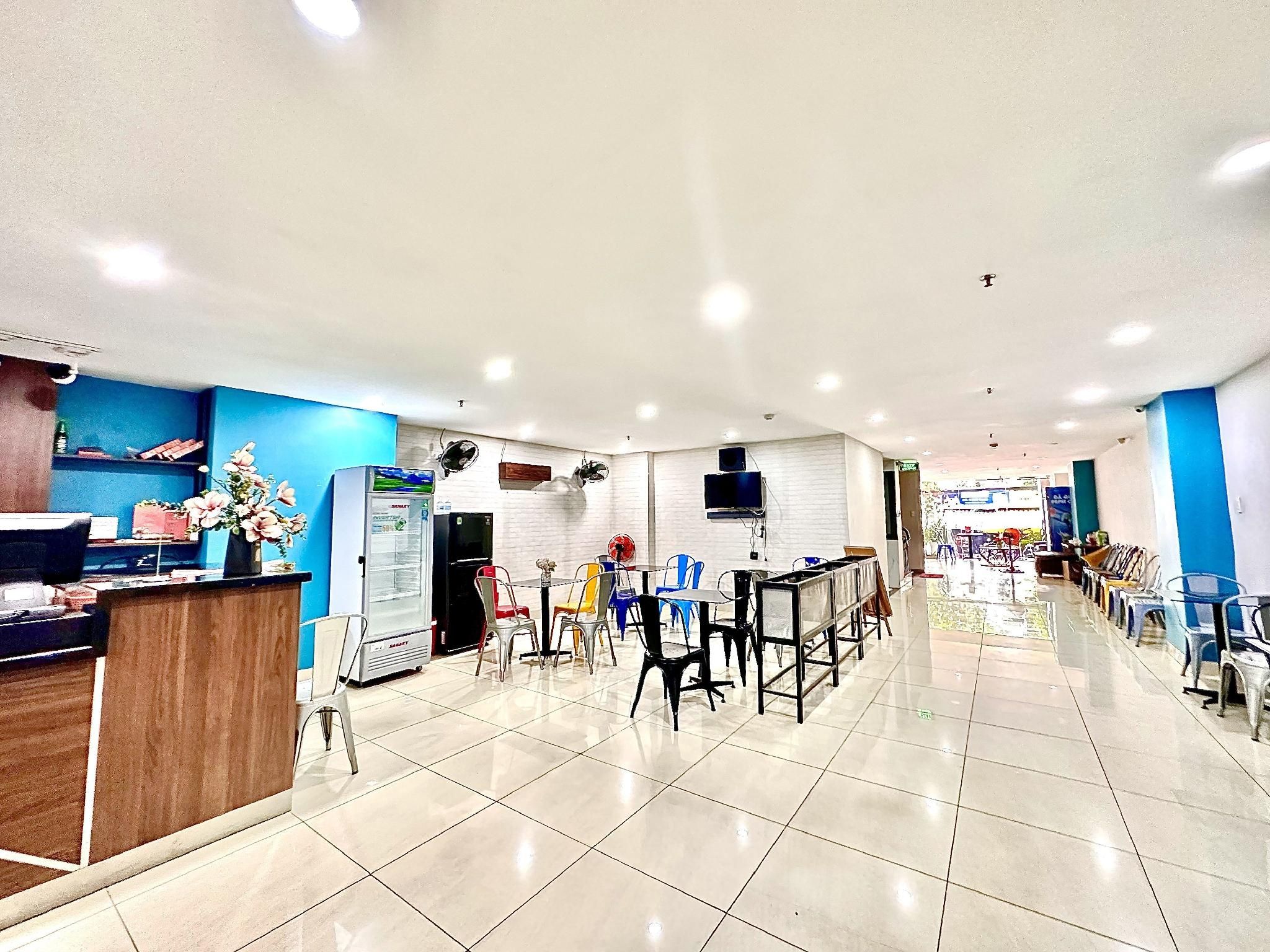 A spacious indoor area with multiple tables and chairs, a refrigerator, and a wall-mounted fan.