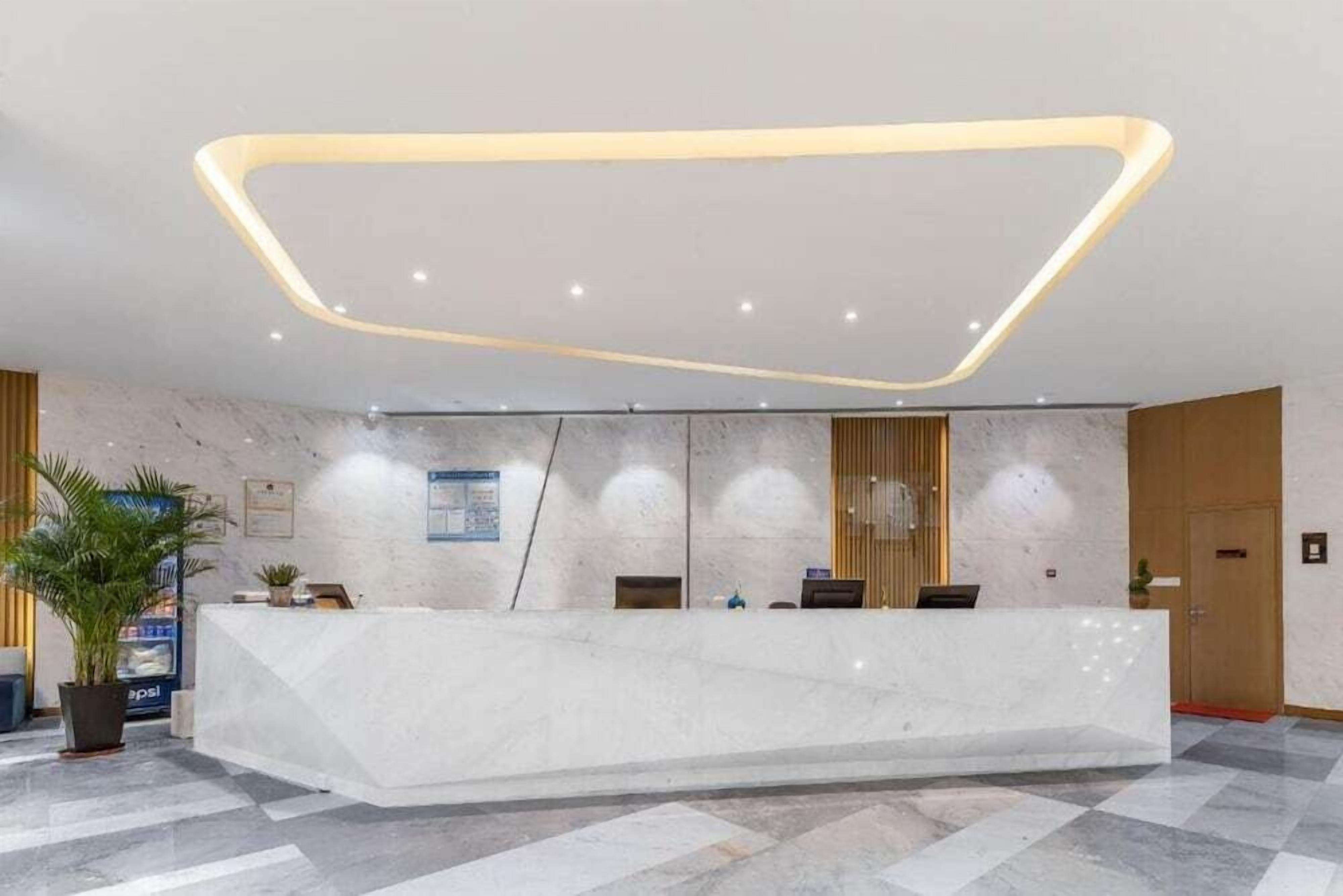 A modern reception area with a marble reception desk, a geometric ceiling light fixture, and a check-in counter.
