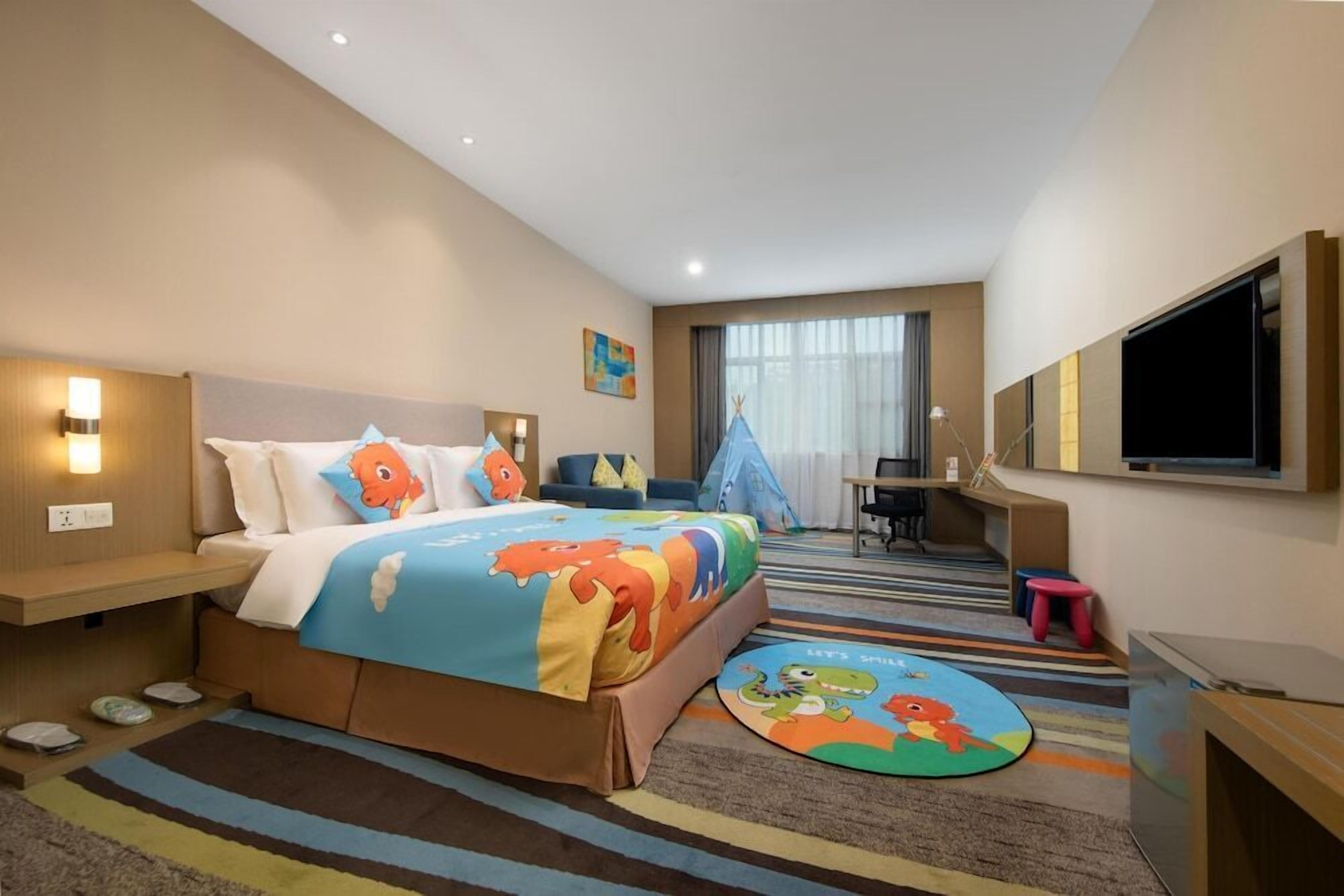 A hotel room with a bed, a desk, a chair, a TV, and a window with curtains.