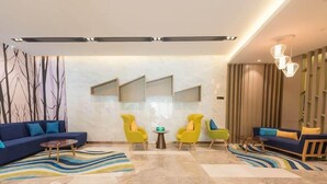 A modern lobby with a blue sofa, yellow chairs, a marble floor, and a decorative wall with vertical panels. - Vyluk Hotel Guangzhou Baiyun International Airport (Guangzhou)