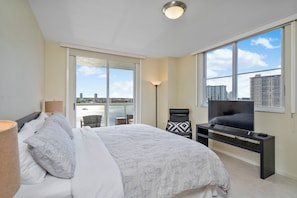 A modern bedroom with a large bed, a TV on a stand, and a view of the city through large windows. - Entire condo in Sunny Isles Beach, Florida, United States (Sunny Isles Beach)