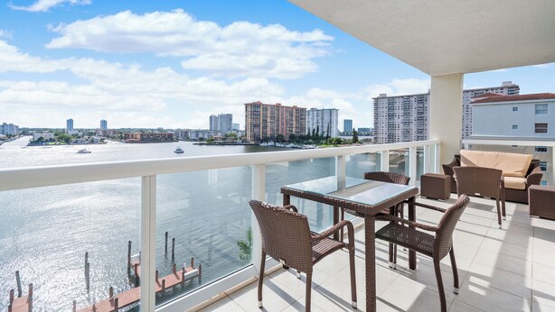 A balcony with wicker furniture overlooking a river with boats and buildings. - Entire condo in Sunny Isles Beach, Florida, United States (Sunny Isles Beach)