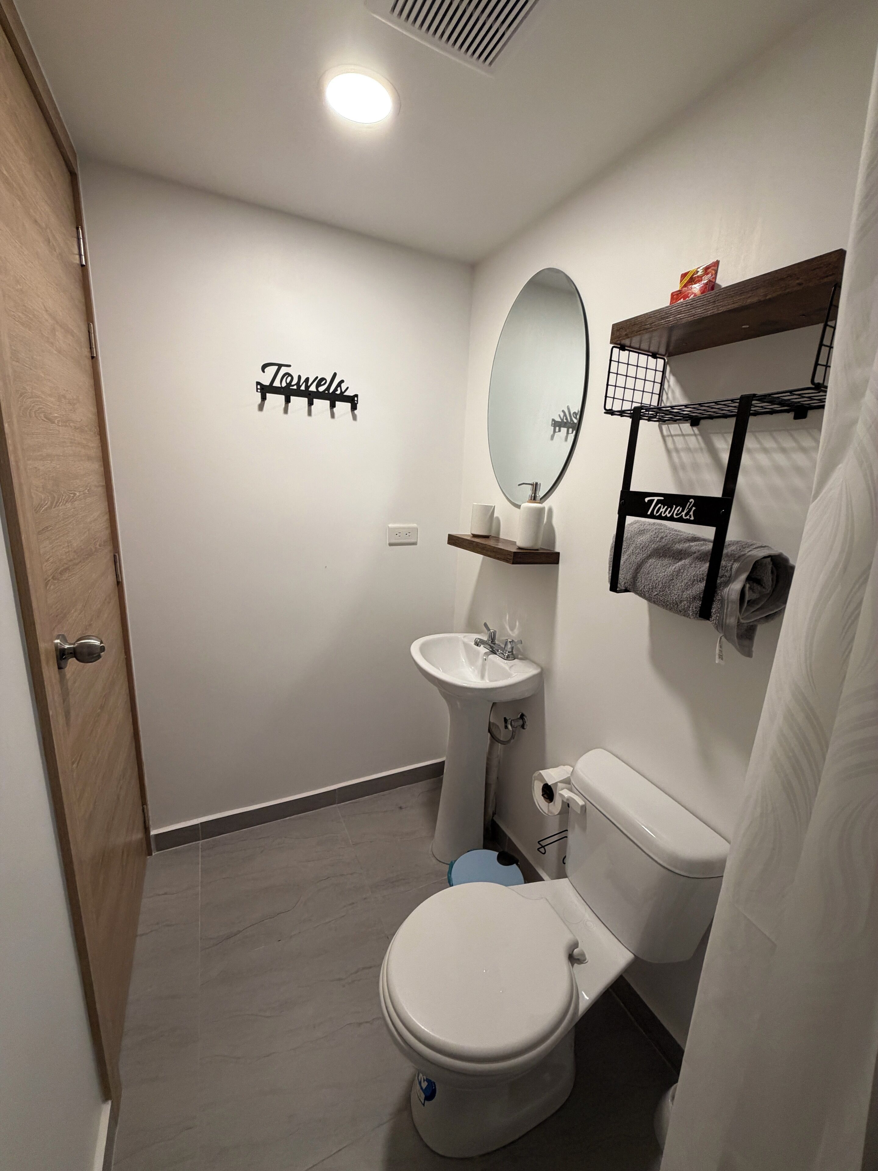 Une salle de bain moderne équipée de toilettes, d’un lavabo et d’un miroir. On y trouve également des crochets pour les serviettes et une étagère avec des articles de toilette.