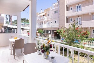 Un balcón con una mesa y sillas, un jarrón con flores y vistas a edificios cercanos.