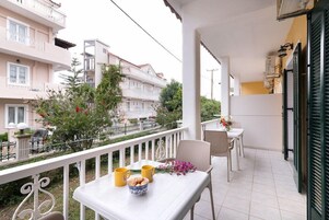 Un balcón con una mesa dispuesta para dos, una silla y un pequeño jardín con plantas y un árbol.
