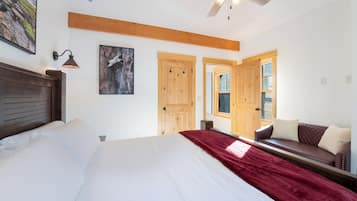 A bedroom with a bed, a red throw blanket, a wooden headboard, a ceiling fan, and a wooden bench with cushions.