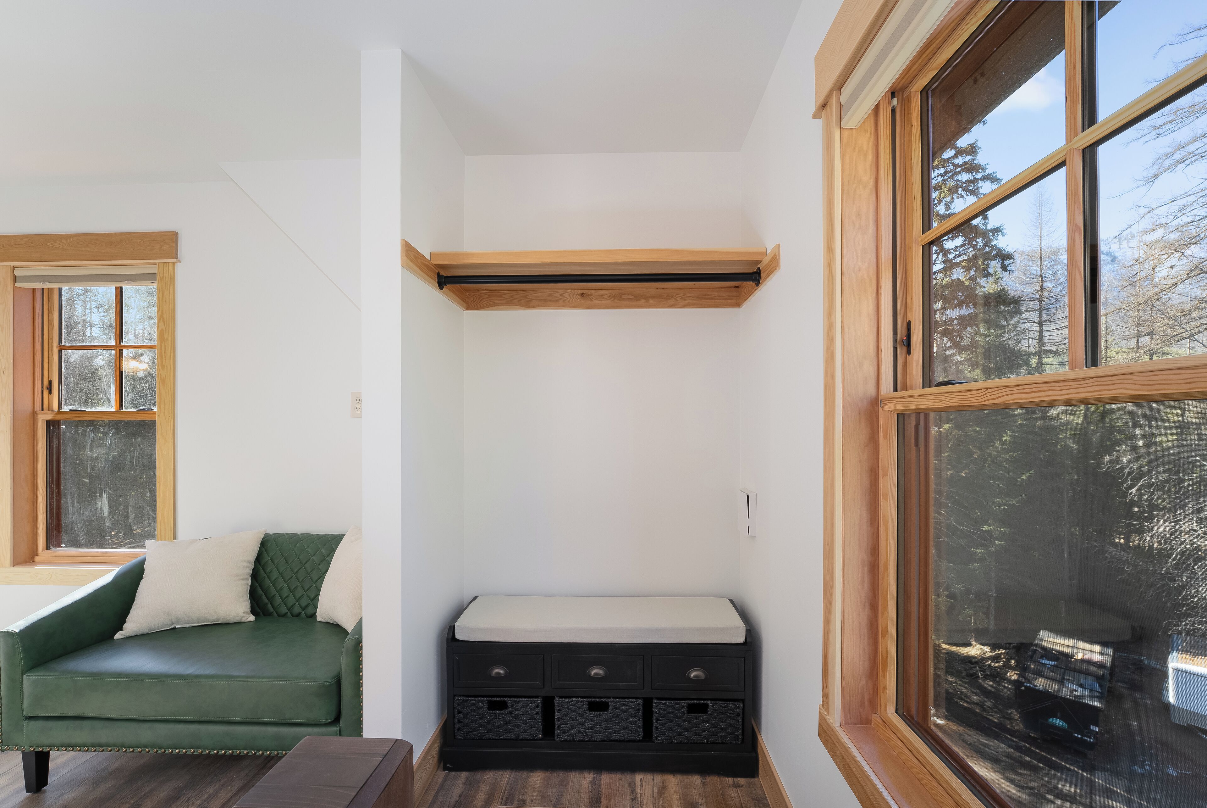 A corner room with a green sofa, a bench with drawers, and a large window with a view of trees.
