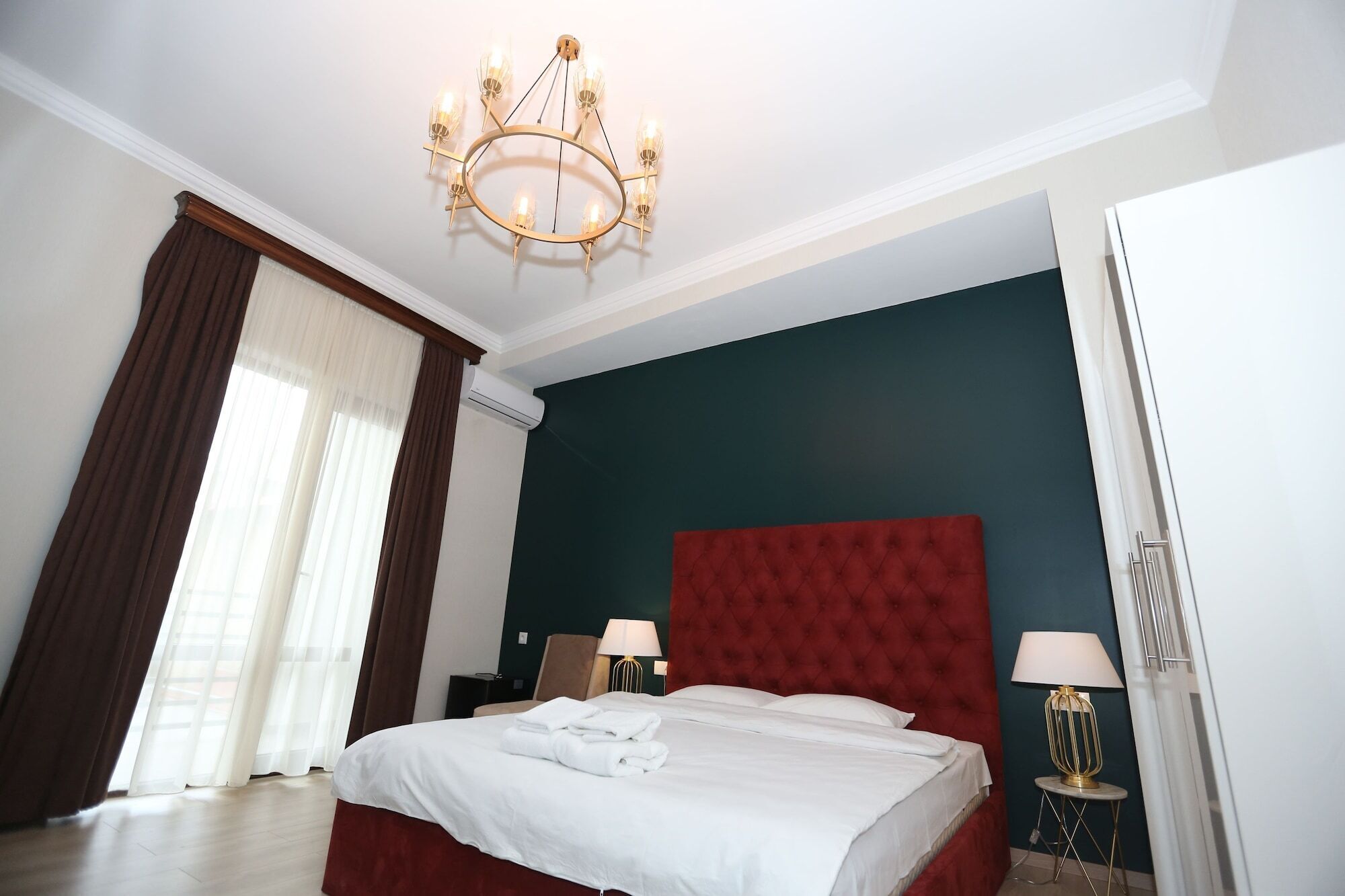 A hotel room with a large bed, a red headboard, two bedside lamps, and a chandelier.