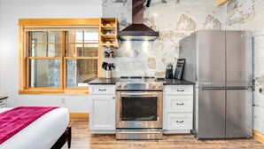 A compact kitchen with a built-in oven, a stainless steel refrigerator, and a window with wooden frames. - New! Lake McDonald Townhome. In Glacier National Park! (West Glacier)