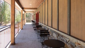 A covered outdoor seating area with tables and chairs, a stone wall, and a view of trees. - New! Lake McDonald Townhome. In Glacier National Park! (West Glacier)