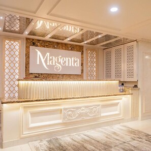 Un comptoir d’accueil avec une enseigne portant le nom « Magenta », un mur orné de motifs et un sol en marbre.