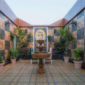 Un patio con una fuente, plantas en macetas y un mural en la pared.