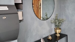 Ein modernes Interieur mit einer grauen, strukturierten Wand, einem schwarzen Konsolentisch mit goldener Schale und einer kleinen Skulptur sowie einem gerahmten Zertifikat auf einem grauen Schrank.