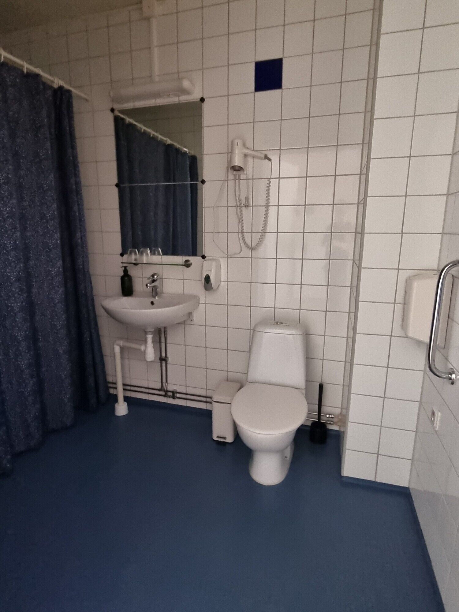 A bathroom with a white sink, a toilet, a shower, and a blue curtain.