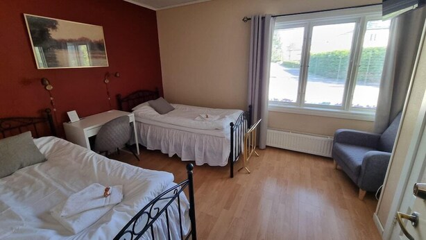 Ein Zimmer mit zwei Betten, einem Schreibtisch und einem Stuhl. Es gibt ein Fenster mit Vorhängen, eine Heizung und ein Bild an der Wand.