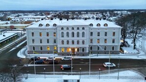 A large, historic building with multiple windows and a central entrance, surrounded by a snowy landscape and other buildings. - Mariestads Stadshotell (Mariestad)