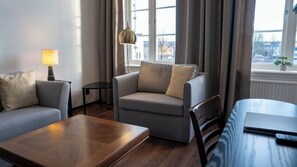 A modern living room with a sofa, armchair, and coffee table, a lamp, and a view through large windows.