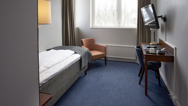 A hotel room with a bed, a desk, a chair, a television, and a window with curtains. - Mariestads Stadshotell (Mariestad)
