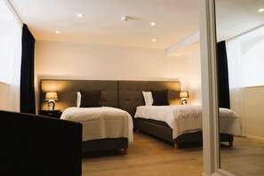 Habitació d'hotel amb dos llits, un capçal gran, làmpades de nit i vista a través d'una porta de vidre.