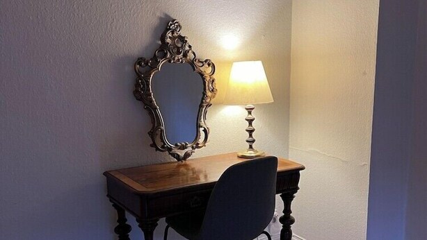 A small, dark wooden desk with a chair and a mirror with an ornate frame. A table lamp is on the desk. - Hotel Sirius (Kristianstad)