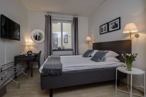 Ein Hotelzimmer mit Bett, Nachttisch, Lampe, Fernseher und Schreibtisch mit Stuhl.