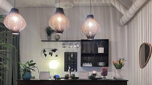 A reception desk with three hanging pendant lights, a world map, a clock, and a mirror on the wall. - Hotel Sirius (Kristianstad)