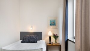 A hotel room with a bed, a bedside lamp, a small table with a vase of flowers, a framed picture on the wall, and a window with curtains. - Hotel Sirius (Kristianstad)