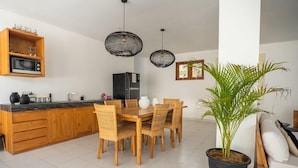 A modern kitchen with wooden cabinetry, a dining table with chairs, and a potted plant. - Ohana's Boutique Resort and Beach Lounge (Lembongan Island)