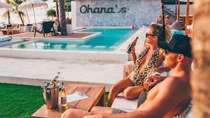 A poolside area with a sign reading "Ohana's", a wooden table with drinks, and lounge chairs. - Ohana's Boutique Resort and Beach Lounge (Lembongan Island)