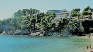 Una zona costanera amb un litoral rocos, aigua turquesa cristal·lina i edificis amb balcons davant del mar.