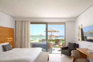 A hotel room with a bed, a desk, a chair, a TV, and a balcony with a view of the beach and umbrellas. - High Beach White - Adults Only (Hersonissos)