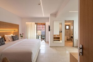 Une chambre d’hôtel moderne avec un grand lit, une tête de lit en bois, une salle de bain avec un miroir et une vue sur le balcon extérieur.
