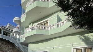 A multi-story building with a stone-paved courtyard, balconies with white railings, and potted plants. - Relax Apartments Saranda (Sarandë)