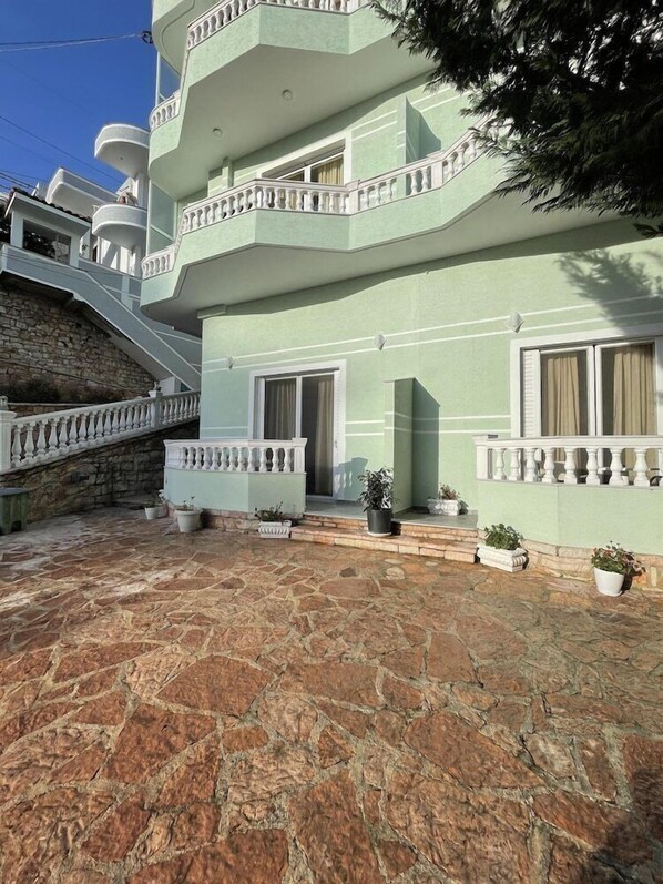 A multi-story building with a stone-paved courtyard, balconies with white railings, and potted plants. - Relax Apartments Saranda (Sarandë)
