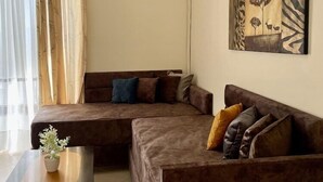 A living room with a brown sectional sofa, a wooden coffee table, and a painting on the wall. - Relax Apartments Saranda (Sarandë)