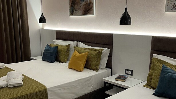 A hotel room with two beds, each with a green bedspread and white linens. There are pillows in various colors, a nightstand with a book, and a painting on the wall. - Relax Apartments Saranda (Sarandë)