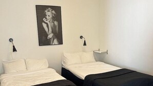 A room with two beds, each with a black bedspread and white pillows. There is a black and white framed picture on the wall above the beds. - Hotel Torslanda Studios (Torslanda)