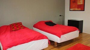 Ein Zimmer mit zwei Einzelbetten, beide mit roter Bettdecke und weißen Kissen. Ein schwarzer Nachttisch und ein roter Teppich liegen auf dem Boden.