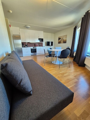 A modern living room with a sofa, a dining table with chairs, a kitchen area, and a TV mounted on the wall. - Hotel Torslanda Studios (Torslanda)