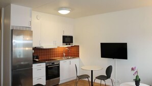 A compact kitchen with white cabinets, a stainless steel refrigerator, a microwave, and a sink. There is a small dining area with two chairs and a table. - Hotel Torslanda Studios (Torslanda)