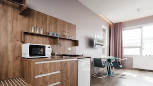 A modern kitchen with a microwave, sink, and wooden cabinetry. There is a dining area with a table and chairs, and a window with curtains. - Hotel Oddsson (Reykjavik)