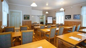 A conference room with wooden tables and chairs, a whiteboard, and framed pictures on the walls.
