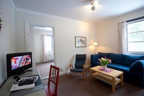 Een woonkamer met een televisie, een blauwe bank, een houten salontafel en een stoel.