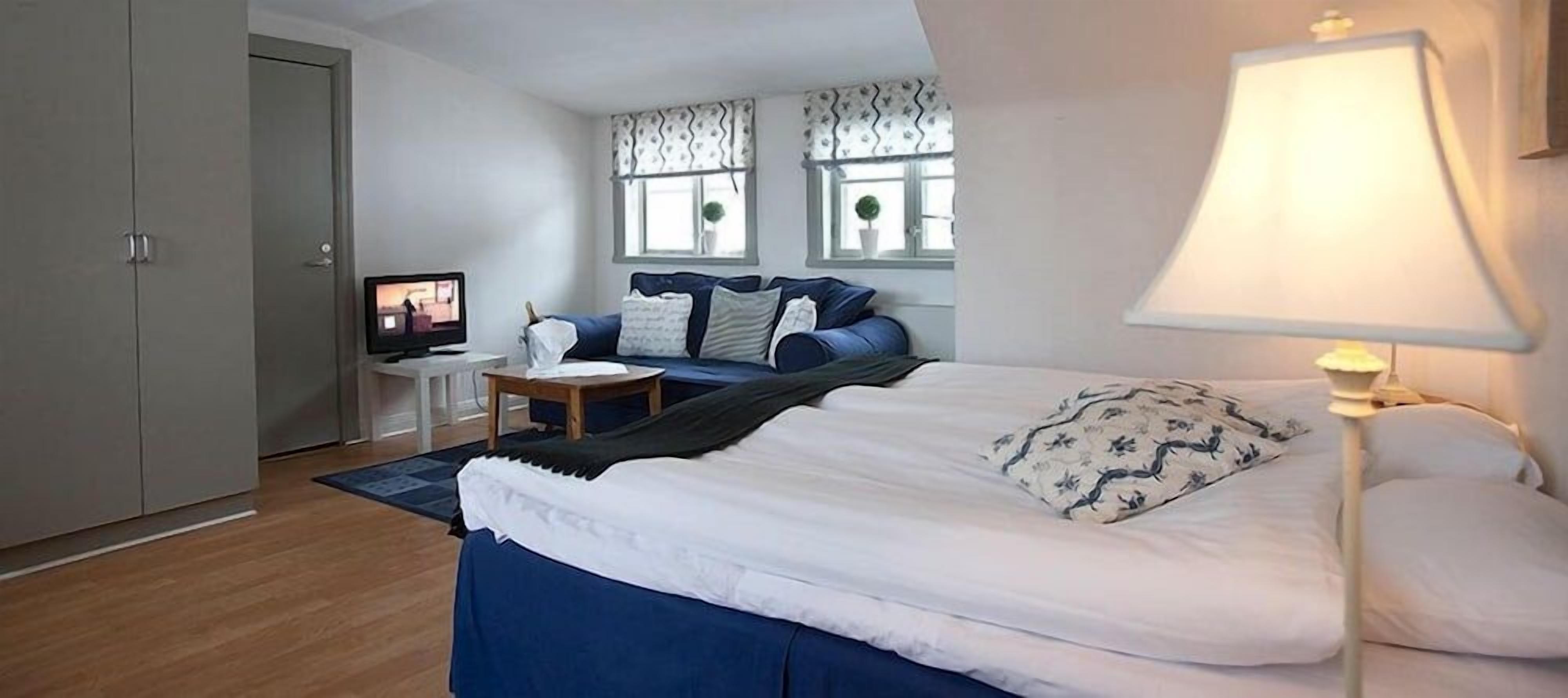 A bedroom with a bed, a desk, a chair, a lamp, and a television.