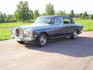 En klassisk Rolls-Royce parkerad på en asfalterad yta med grönska i bakgrunden.