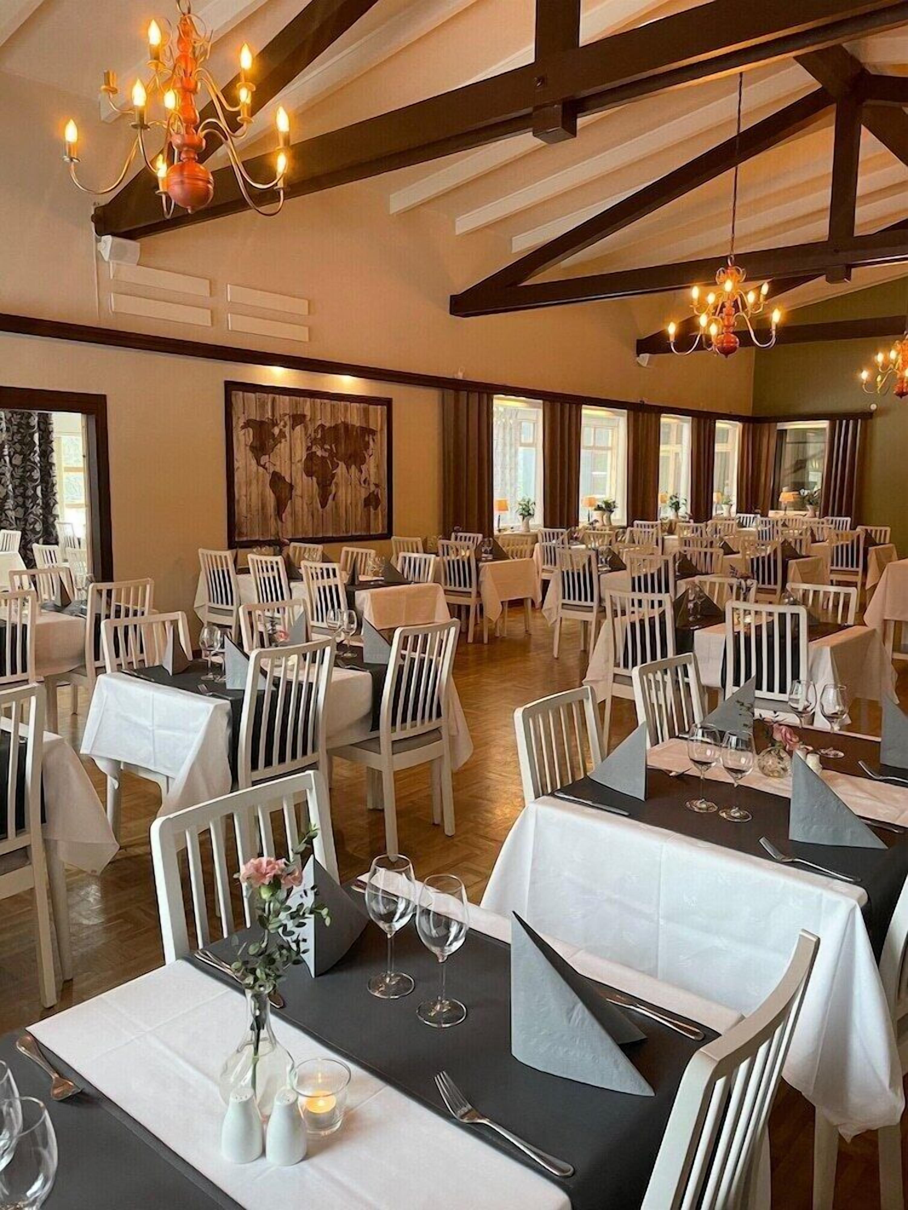 A restaurant with white chairs and tables, chandeliers, and a large painting on the wall.