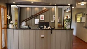 A reception desk with a wooden staircase in the background, a black telephone, and a small sign on the desk. - Hotel Mullsjö (Mullsjö)