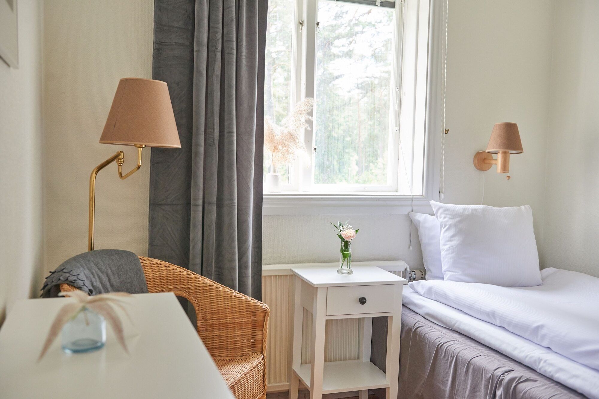 A bedroom with a bed, a nightstand, a chair, a lamp, and a window with curtains.