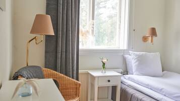 A bedroom with a bed, a nightstand, a chair, a lamp, and a window with curtains.