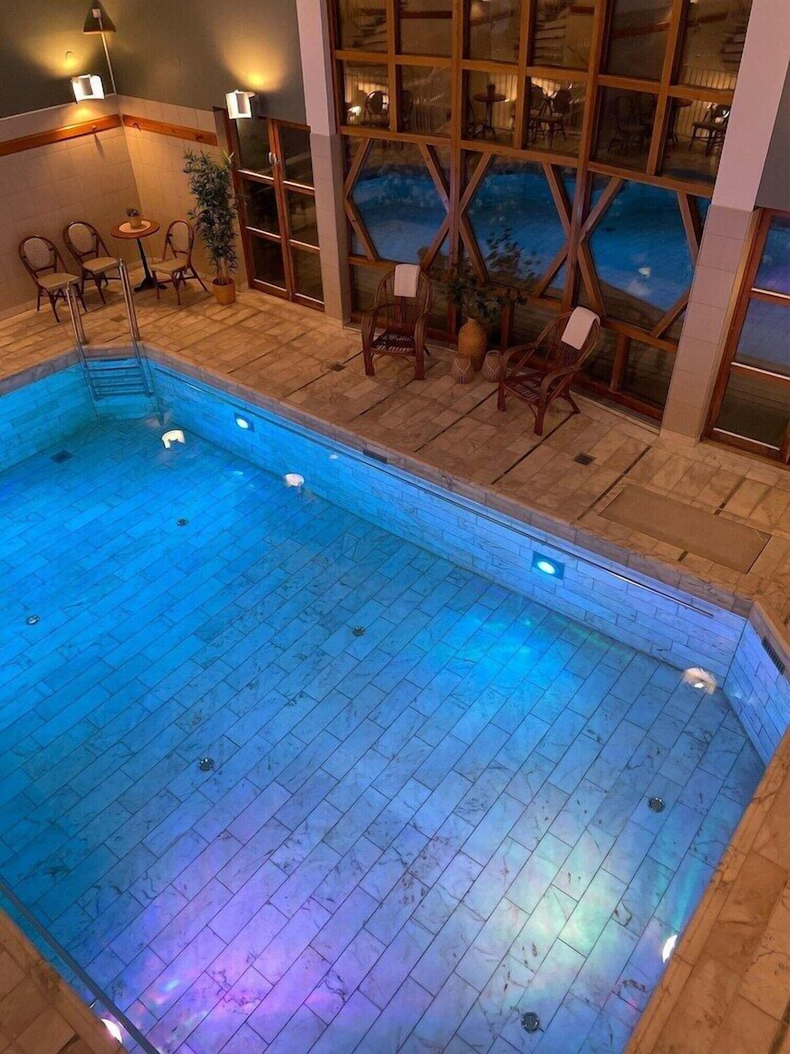 Ein überdachter Pool mit gefliestem Boden und einer Holzterrasse mit Stühlen und Tischen.